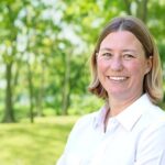 A professional headshot of Jessica Ellison, MS, CPE, CSP, wearing a white collared shirt against a blurred outdoor green background.